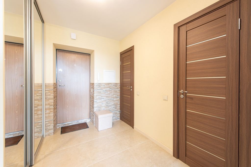 Entree a Bordeaux carrelee en beige, parement effet pierre et portes bois fonce, renovation par MC Carreleur.