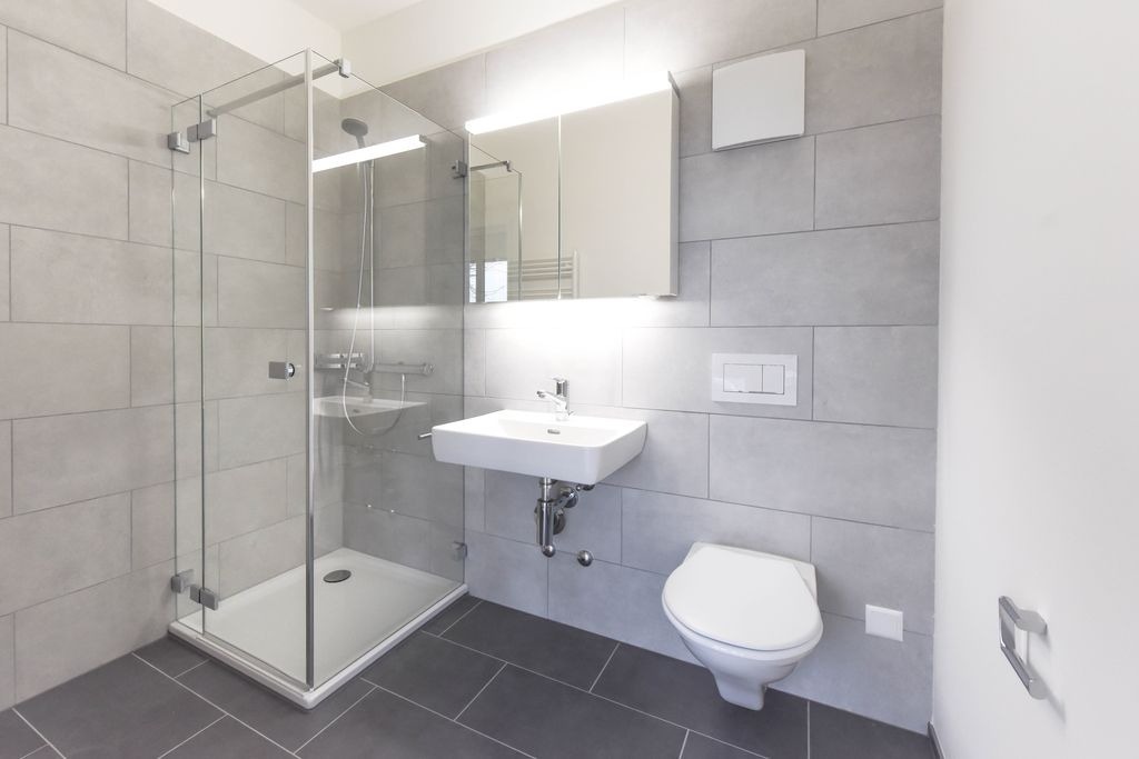 Salle de bain moderne en carrelage grand format a Izon par MC Carreleur, murs gris clair, sol fonce et douche walk-in.