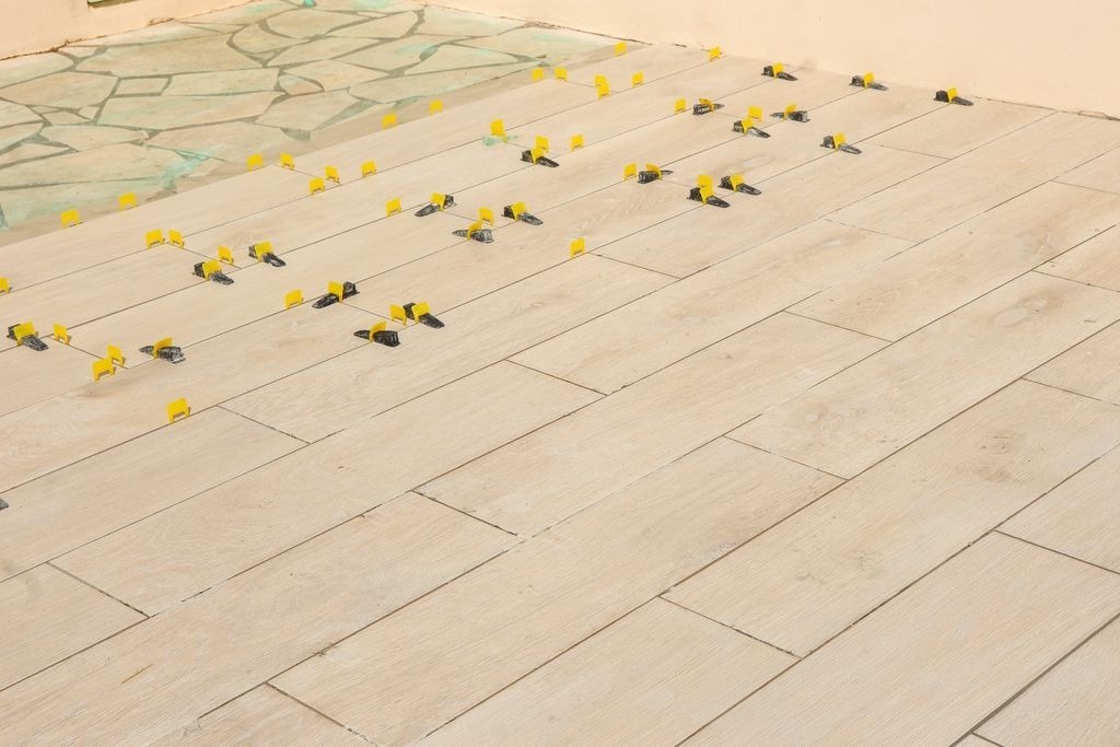 Carrelage imitation bois clair en cours de pose en veranda a Libourne, avec systeme autonivelant par MC Carreleur.